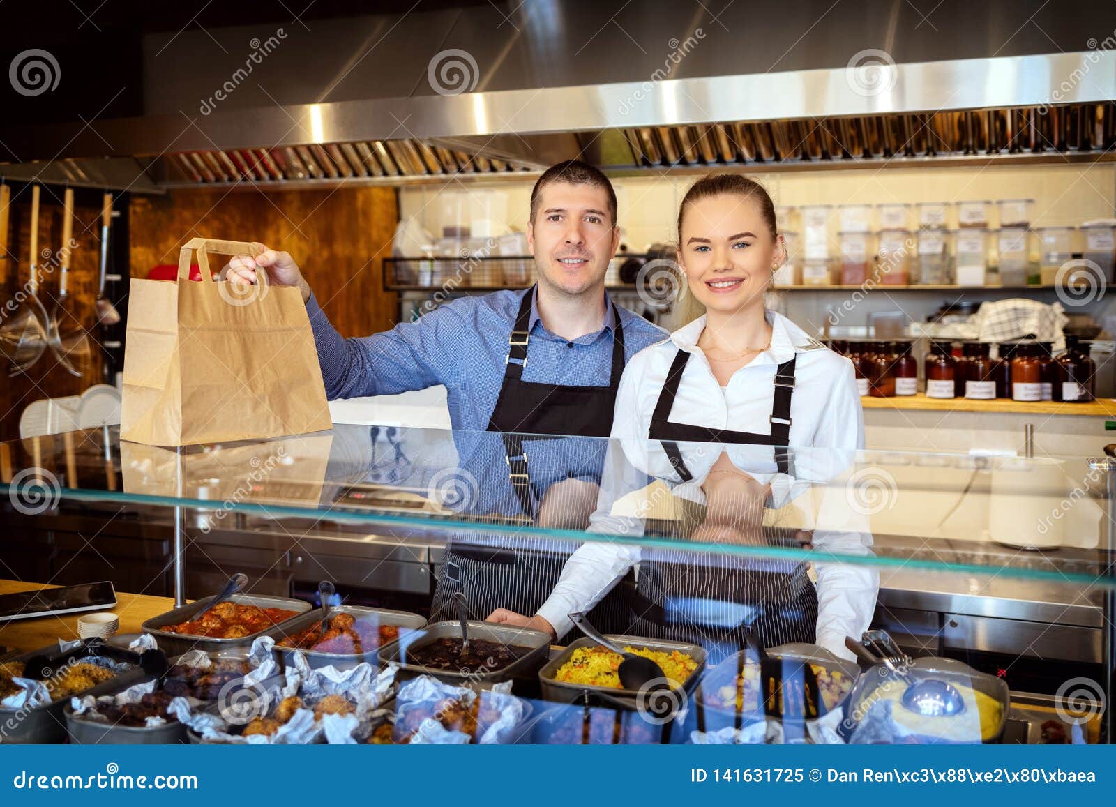 portrait of small business owner smiling behind counter inside eatery holding food order for home delivery